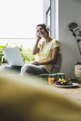 Woman listening music on headphones at home - UUF24561