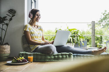 Woman looking away while sitting with laptop at home - UUF24563