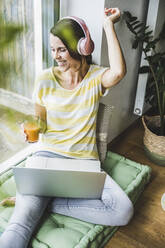 Woman listening music holding juice while sitting at home - UUF24568