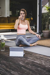 Woman drinking detox water while sitting cross-legged on terrace - UUF24582