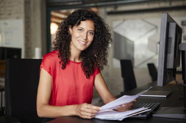 Weibliche Fachkraft hält ein Dokument, während sie im Büro sitzt - RBF08217