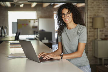 Berufstätige Frau, die am Schreibtisch sitzend einen Laptop benutzt - RBF08244