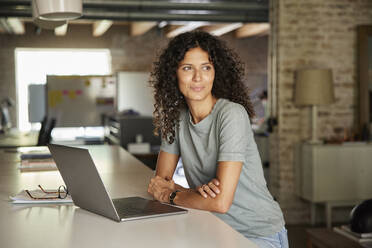 Thoughtful businesswoman looking away while sitting with laptop at workplace - RBF08245