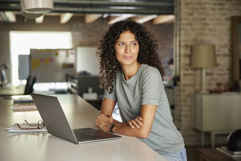 Nachdenkliche Geschäftsfrau, die mit ihrem Laptop am Arbeitsplatz sitzt und wegschaut - RBF08245