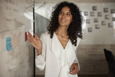 Smiling businesswoman examining strategy at whiteboard in office - RBF08255