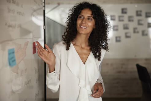 Lächelnde Geschäftsfrau, die eine Strategie am Whiteboard im Büro prüft - RBF08255