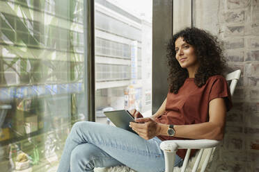 Geschäftsfrau hält digitales Tablet und sitzt am Fenster - RBF08268