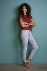 Smiling woman with arms crossed leaning on turquoise wall - RBF08274