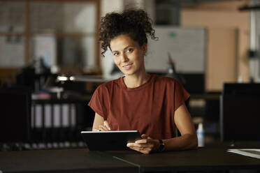 Smiling businesswoman with digital tablet at desk - RBF08286
