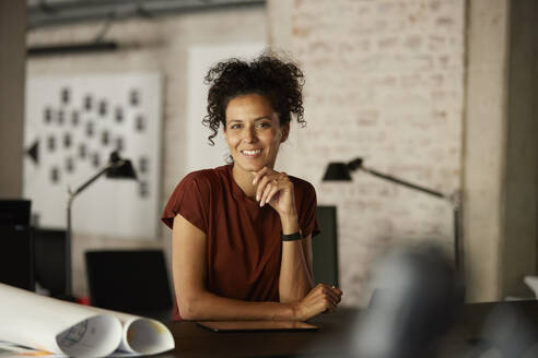 Female professional with hand on chin leaning at workplace - RBF08288