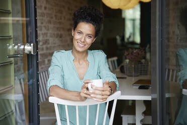 Smiling businesswoman holding coffee cup while sitting on chair - RBF08298