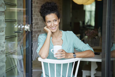 Nachdenkliche Frau, die eine Kaffeetasse hält und auf einem Stuhl sitzt - RBF08299