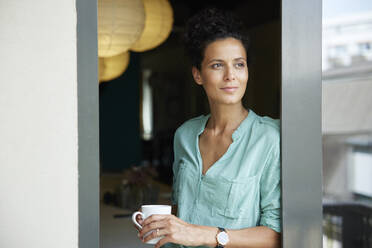 Businesswoman holding coffee cup leaning on door - RBF08300