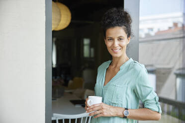 Lächelnde weibliche Fachkraft, die eine Kaffeetasse hält und sich an die Tür lehnt - RBF08303