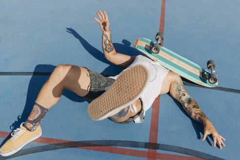 Fallen young man with skateboard on face at basketball court during sunny day - JRVF01358