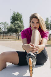 Beautiful blond woman wearing inline skate sitting on bench during sunny day - JRVF01378