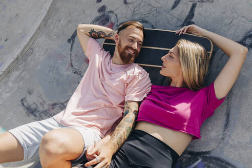 Junges Paar sieht sich an, während es im Skateboardpark liegt - JRVF01379