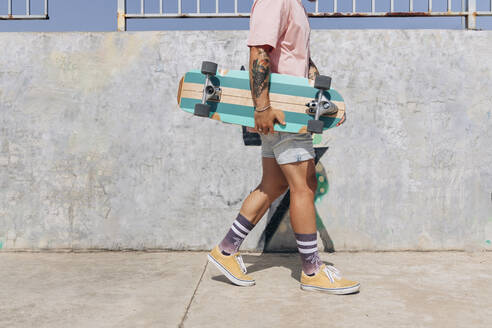 Junger Mann mit Skateboard auf dem Fußweg an einem sonnigen Tag - JRVF01383