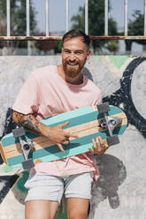 Fröhlicher junger Mann mit Skateboard und Hupzeichen an einem sonnigen Tag - JRVF01384