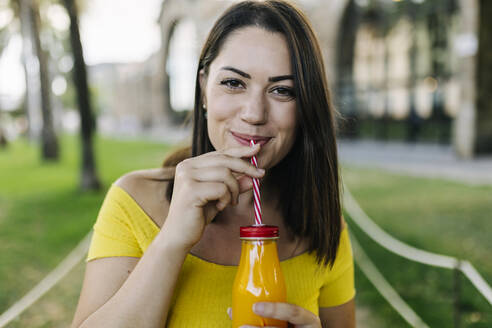 Young woman drinking orange juice from bottle at park - XLGF02145