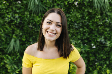 Smiling young woman in front of hedge - XLGF02152