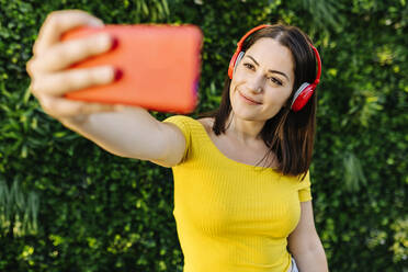 Lächelnde Frau, die ein Selfie mit ihrem Smartphone macht, während sie Musik hört - XLGF02157