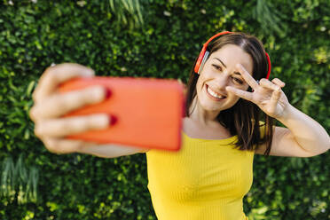 Happy woman gesturing while taking selfie through mobile phone - XLGF02158