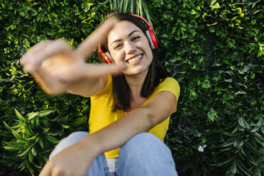 Glückliche junge Frau, die ein Friedenszeichen macht, während sie über Kopfhörer Musik hört - XLGF02164