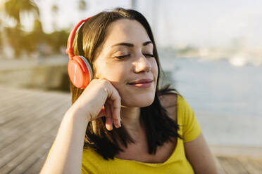Lächelnde Frau hört mit geschlossenen Augen Musik über Kopfhörer - XLGF02167