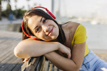 Young woman listening music through headphones while leaning on bench - XLGF02168