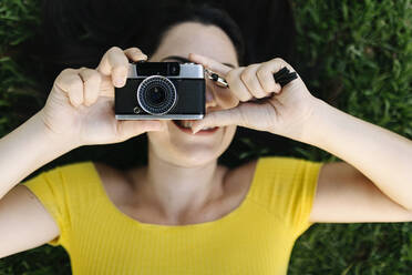 Junge Frau fotografiert durch die Kamera, während sie im Gras liegt - XLGF02173