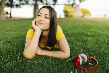 Young woman day dreaming while lying by headphones in lawn - XLGF02183