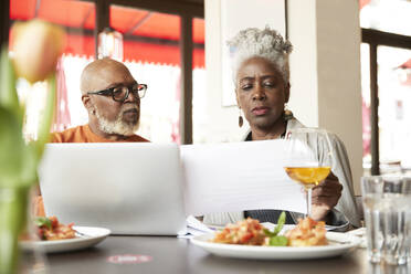 Ältere Frau prüft Papier, während sie mit einem Mann im Restaurant diskutiert - PMF02049