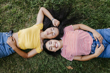 Happy young woman lying with female friend on grass in park - TCEF02059