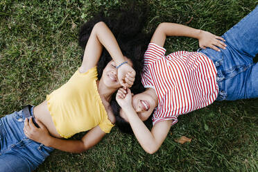 Lächelndes lesbisches Paar, das die Augen mit den Händen bedeckt, während es im Park im Gras liegt - TCEF02061