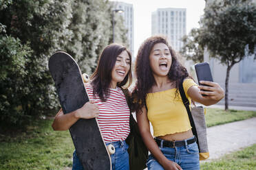 Junge Frau nimmt Selfie durch Smartphone mit weiblichen Freund hält Skateboard im Park - TCEF02070