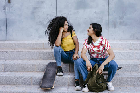 Smiling lesbian couple looking at each other while sitting on steps - TCEF02071