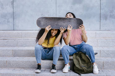 Verspielte Freundinnen sitzen mit Skateboard auf Stufen - TCEF02072