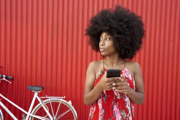 Frau hält Handy, während sie vor einer roten Wand steht - VEGF04818
