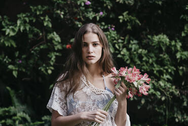 Junge Frau hält Blumenstrauß vor Efeupflanzen - DSIF00535