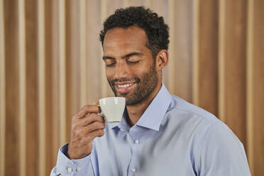 Lächelnde männliche Fachkraft hält Kaffeetasse im Büro - AKLF00381