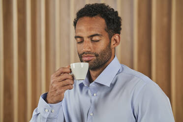 Geschäftsmann riecht Kaffeeduft aus einer Tasse im Sitzungssaal - AKLF00382