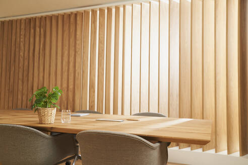 Conference table in front of wooden blinds at office - AKLF00384