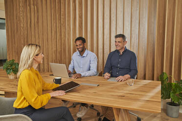 Businesswoman holding digital tablet discussing with male colleagues in board room - AKLF00385