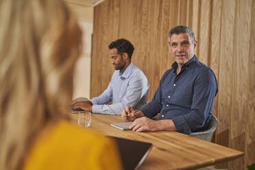 Männlicher Berufstätiger im Gespräch mit einer Mitarbeiterin, während er neben einem Geschäftsmann im Sitzungssaal sitzt - AKLF00388
