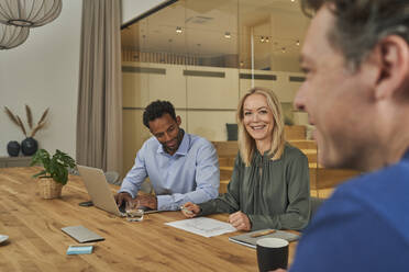 Smiling businesswoman looking at colleague while sitting by businessman in board room - AKLF00408