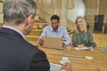 Smiling colleagues discussing during meeting at conference table in board room - AKLF00418