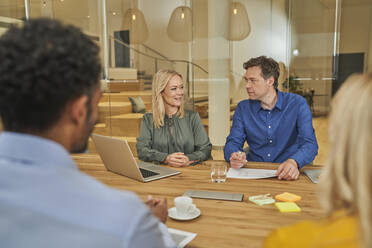 Male and female colleagues discussing while sitting in meeting at office - AKLF00427