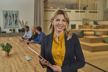 Blond businesswoman holding digital tablet while standing in board room - AKLF00438
