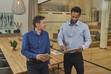 Männlicher Berufstätiger, der ein digitales Tablet benutzt und mit einem Kollegen im Sitzungssaal des Büros diskutiert - AKLF00441